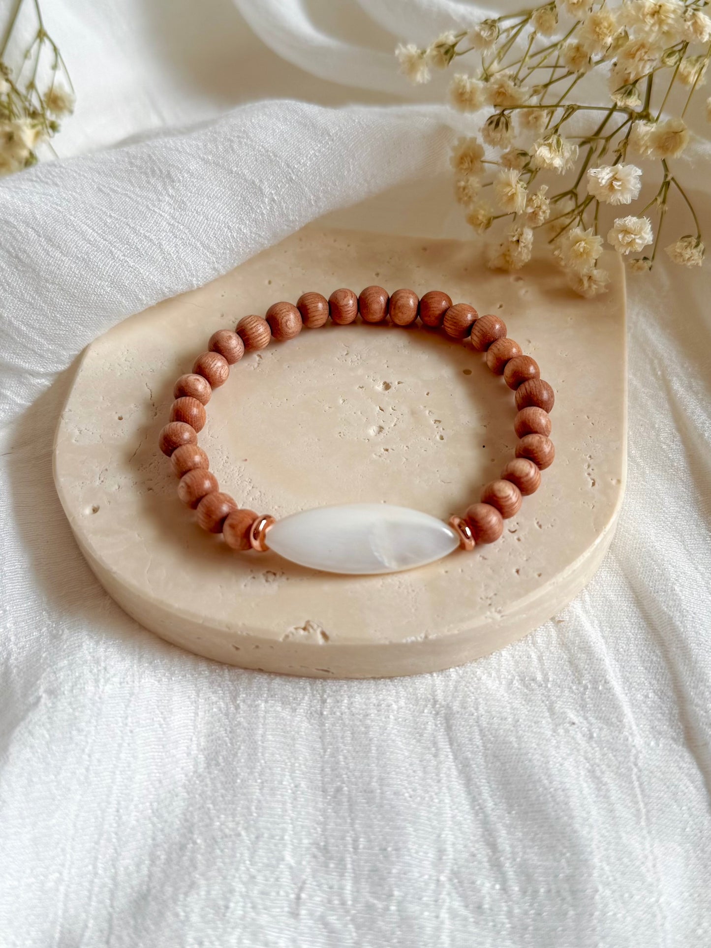 Boho-style gemstone bracelet featuring warm Rosewood beads with a luminous Mother of Pearl focal bead at the center, laid on a neutral fabric background