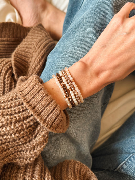 Five handcrafted gemstone bracelets from the Café Mocha Set arranged on a neutral-toned surface. The bracelets feature warm, earthy tones with subtle sparkling accents, evoking cozy fall vibes and comforting coffee and cocoa hues.