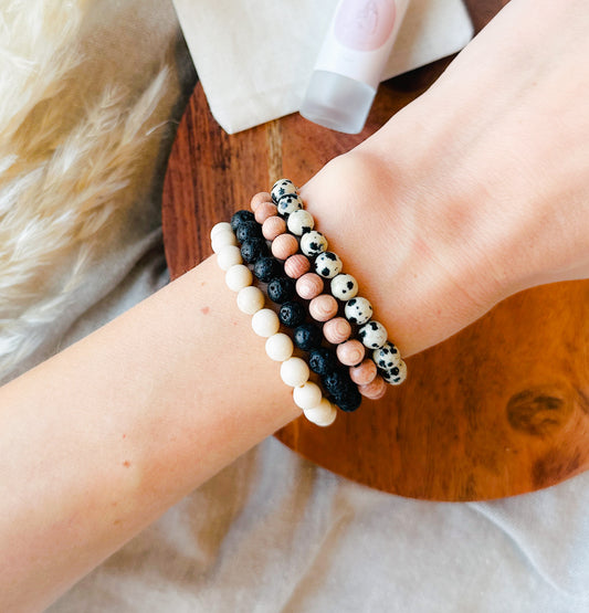 Embark on a journey of wellness with our exquisite Gemstone Bracelet Stack, meticulously crafted to complement our essential oil rollers. This thoughtfully curated stack incorporates the healing properties of Lava Rock, providing a grounding foundation, Rosewood for its soothing embrace, Dalmatian Jasper to infuse joy and playfulness, and Riverstone Jasper to instill tranquility.