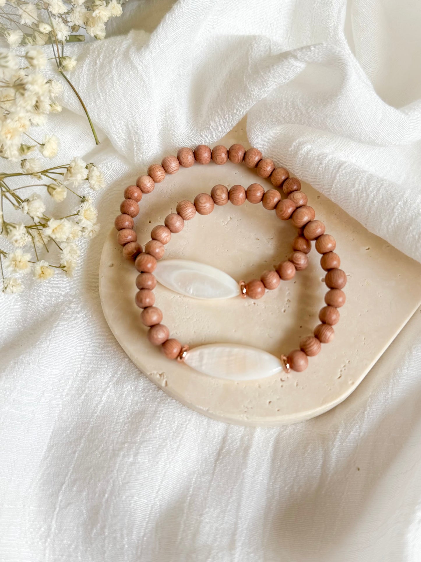 Boho-style gemstone bracelet featuring warm Rosewood beads with a luminous Mother of Pearl focal bead at the center, laid on a neutral fabric background