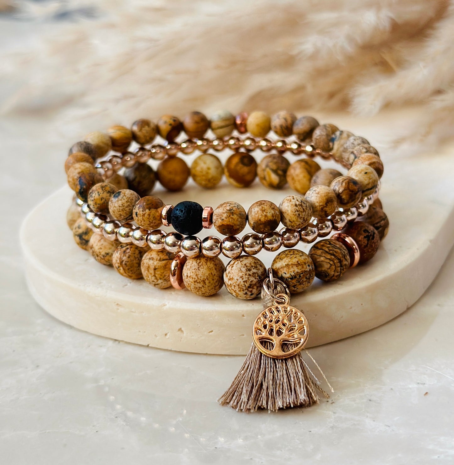 "The Sand Jasper Stack”  a unique gemstone bracelet ensemble meticulously crafted with the soothing and grounding qualities of Sand Jasper, a profound tree of life charm that embodies rich symbolism, and a practical tassel designed to infuse your days with the therapeutic fragrances of essential oils.