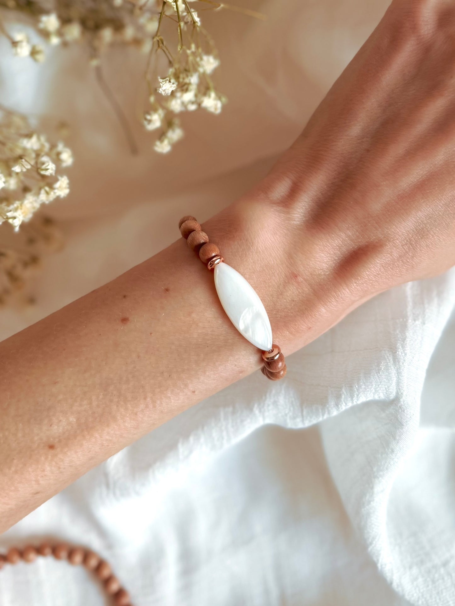 Boho-style gemstone bracelet featuring warm Rosewood beads with a luminous Mother of Pearl focal bead at the center, laid on a neutral fabric background