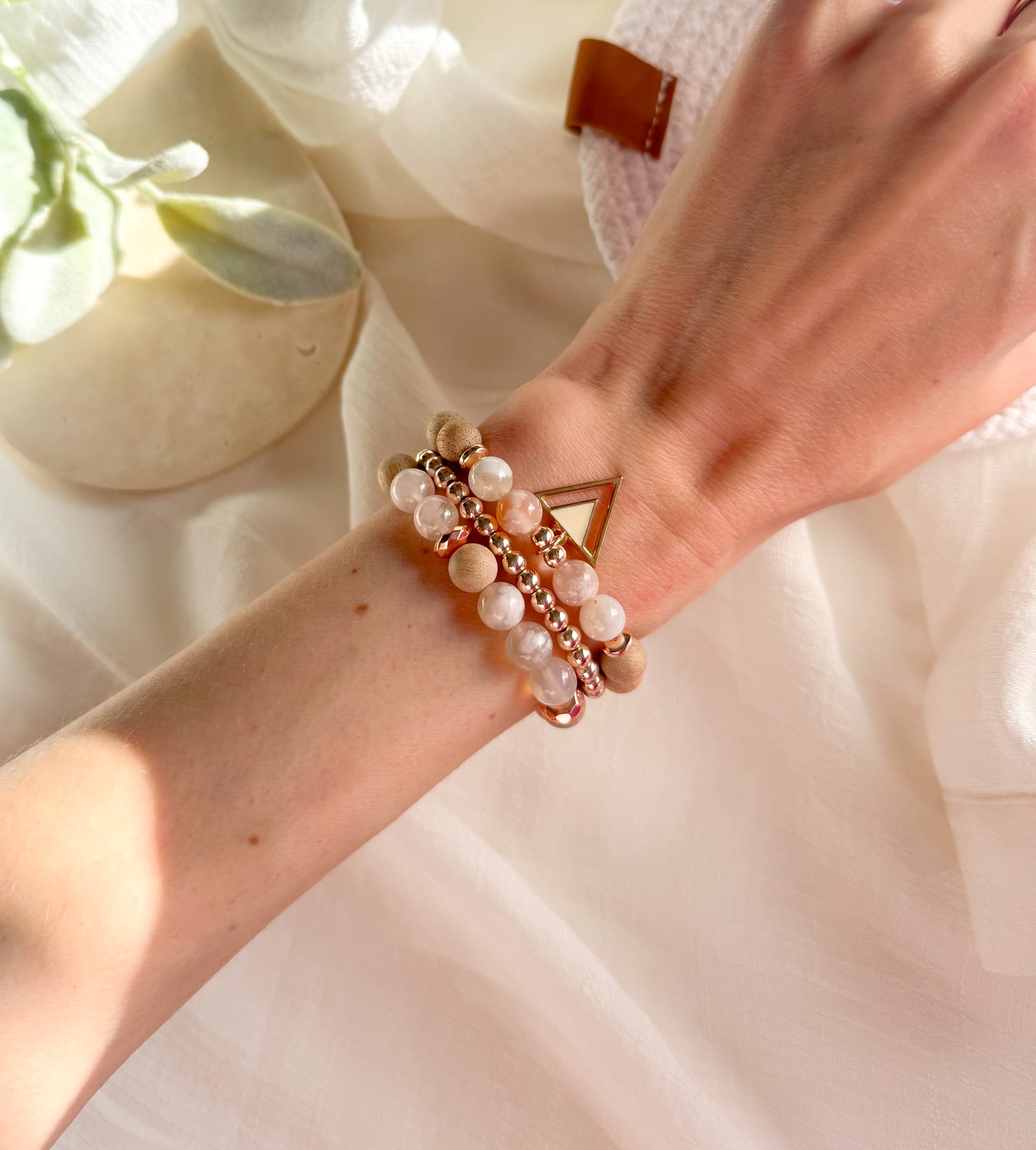 A delicate gemstone bracelet featuring soft pink and white Flower Agate beads, warm Matte Beechwood accents, and a triangle charm. The design is inspired by cherry blossoms, symbolizing renewal and fleeting beauty. The bracelet embodies growth, transformation, and harmony with nature.
