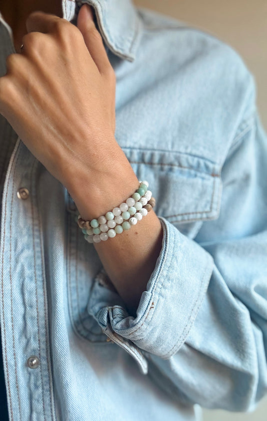A handmade beaded bracelet featuring a soothing mix of gemstones and wood. Pale blue-green Amazonite beads, soft green Jade, warm brown Camphor Wood, and textured white Lava Rock are strung together, creating a design that feels calming, grounding, and timeless.