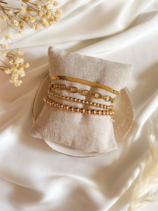 Gold bracelets on a textured beige pillow with a soft white background
