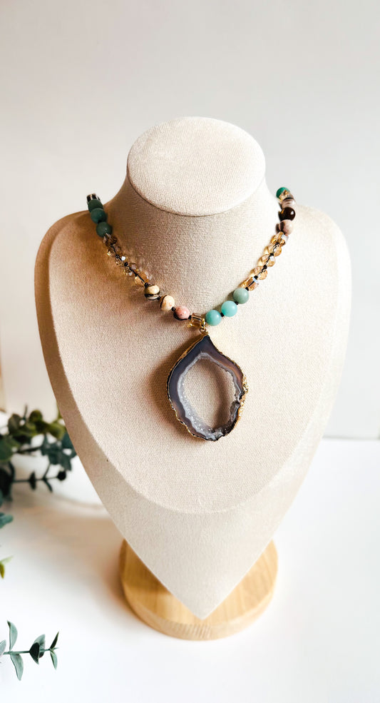 A boho-style necklace named The Odessa Necklace, inspired by the ocean’s rhythmic waves and serenity. It features soothing Amazonite beads, earthy Sandstone, and radiant gold glass beads, creating a harmonious blend of land and sea. At its center, a shimmering Druzy Agate pendant reflects the beauty of sunlit tide pools and hidden ocean treasures. A symbol of tranquility and strength, this handcrafted piece embodies the ebb and flow of nature.