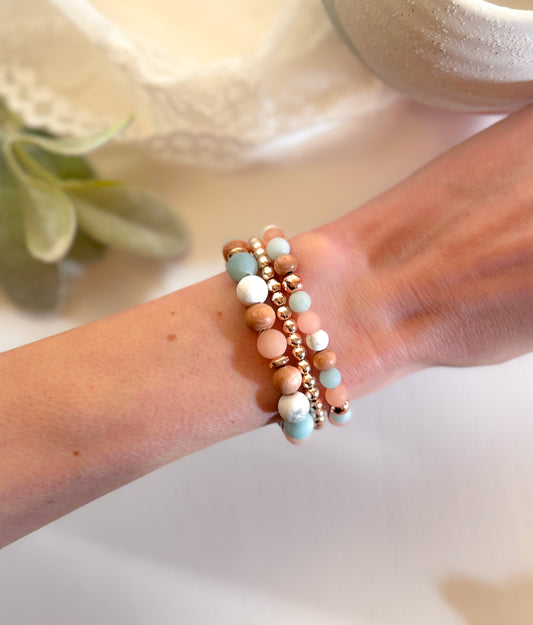 A stack of gemstone bracelets featuring Sunstone, Amazonite, Howlite, and Rosewood beads. The bracelets combine warm and cool tones, with natural wood accents. Designed to boost confidence, uplift energy, and promote balance, the stack blends healing properties with stylish elegance.