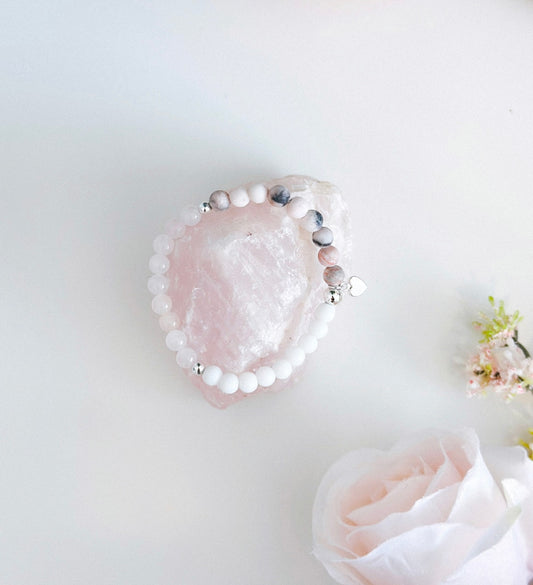 This exquisite gemstone bracelet blends the soothing energies of frosted Pink Zebra Jasper, the love-infused essence of Rose Quartz, and the calming properties of white agate. Crafted with care, it features a delicate silver heart charm, adding a touch of elegance to its design.