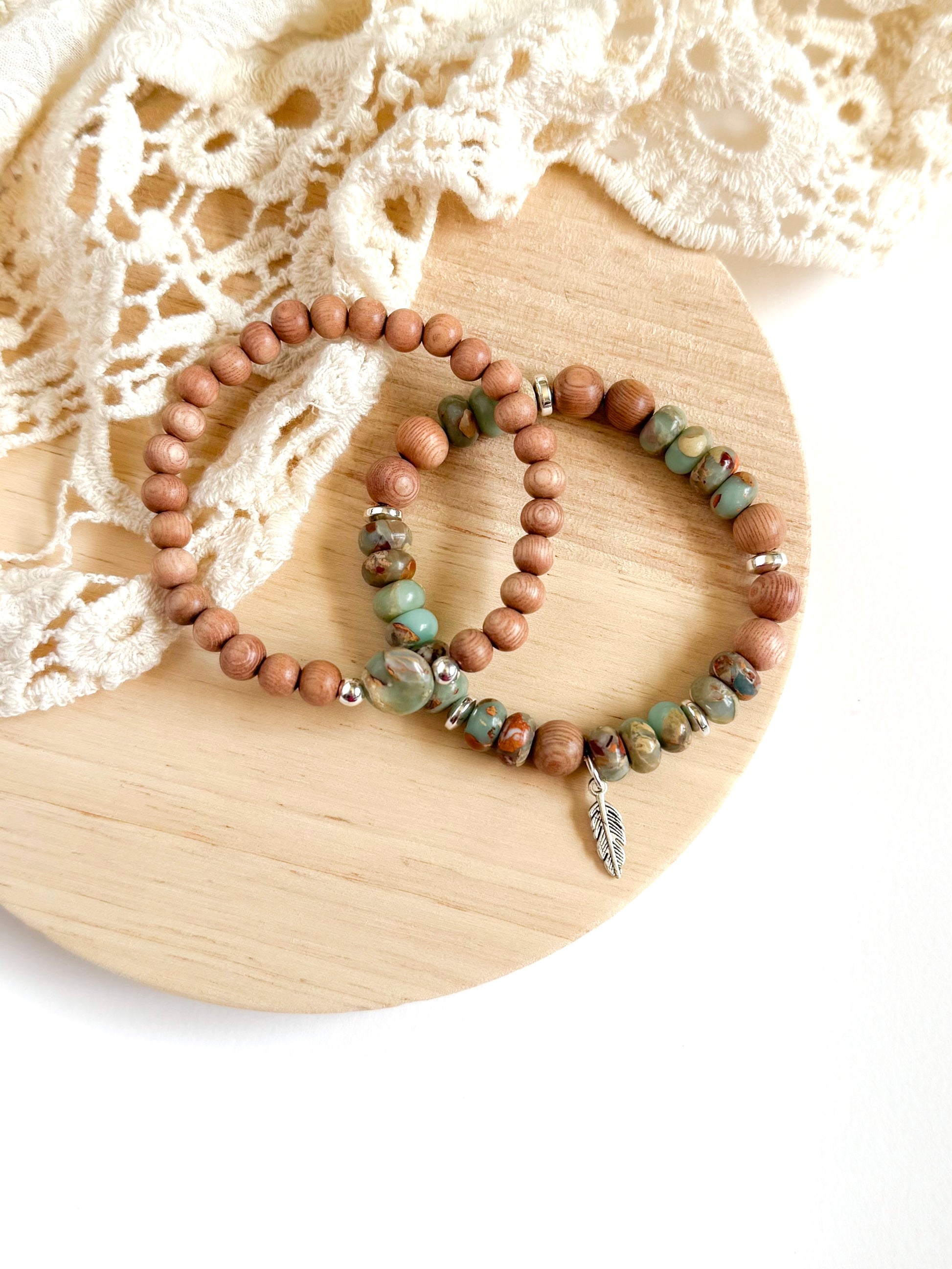 A handcrafted bracelet set featuring Serpentine Jasper beads in earthy green tones, symbolizing transformation and inner peace. Warm, natural Rosewood beads provide grounding energy, while a delicate feather charm dangles, representing freedom and intuition. Designed for free spirits and wanderers, this set embodies balance, resilience, and adventure.