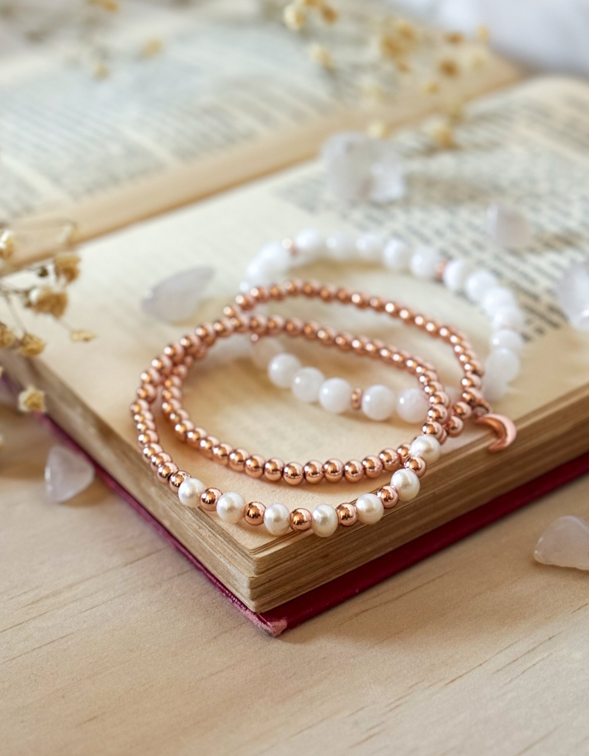 Two pearl and rose gold bracelets on an open book with a soft background