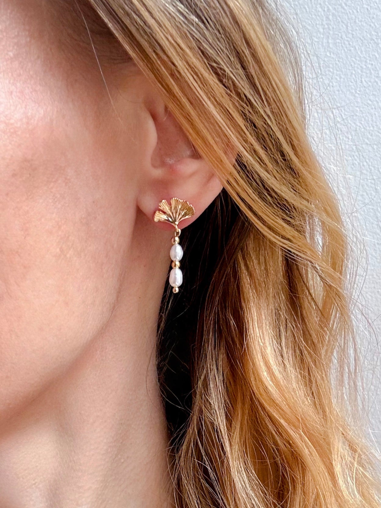 Close-up of a person wearing a gold earring with pearl-like stones against a neutral background.