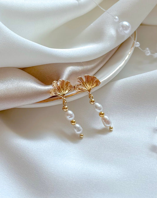 Gold earrings with pearl drops on a white fabric background