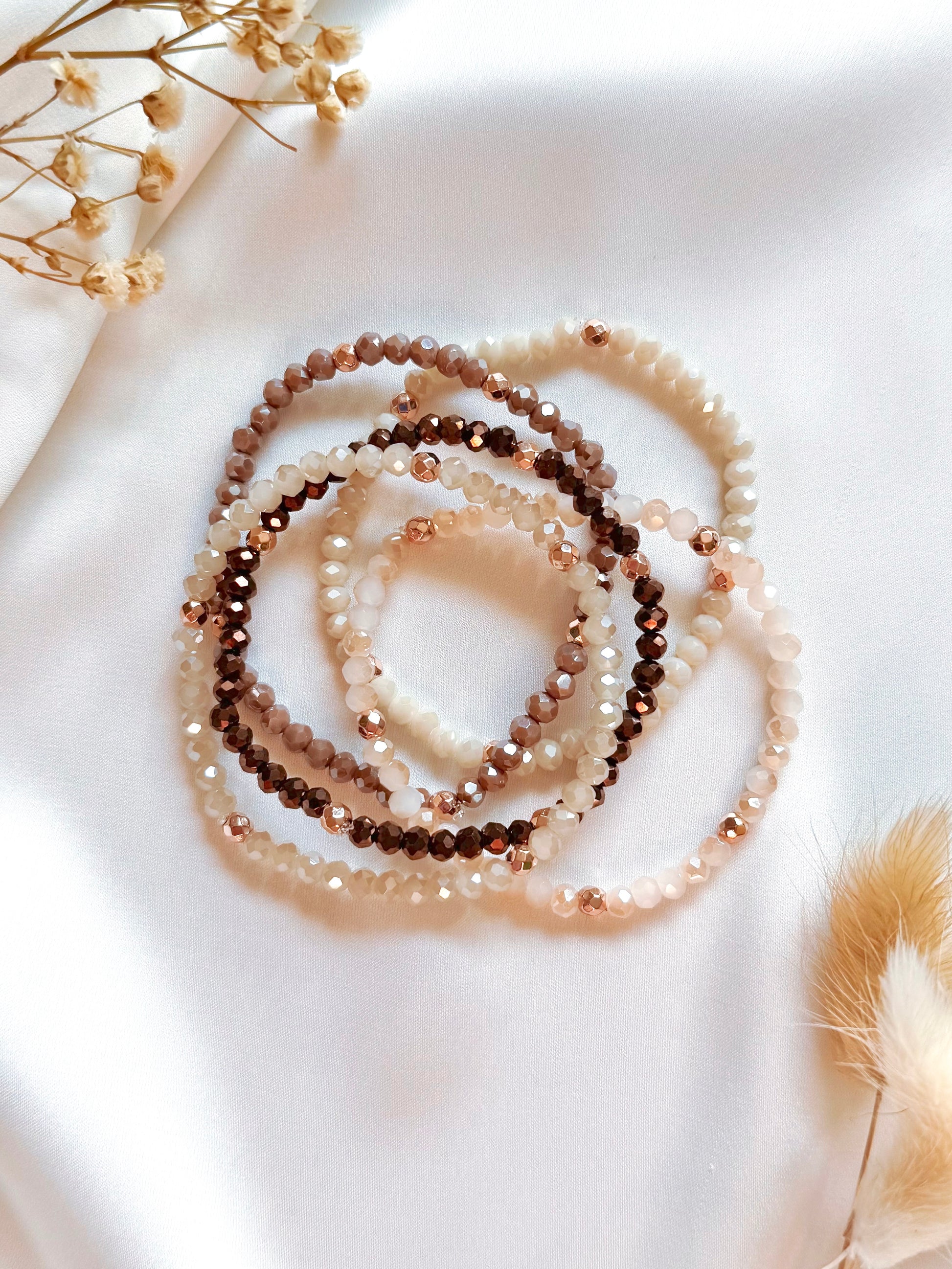 Three beaded bracelets on a light surface with dried flowers.