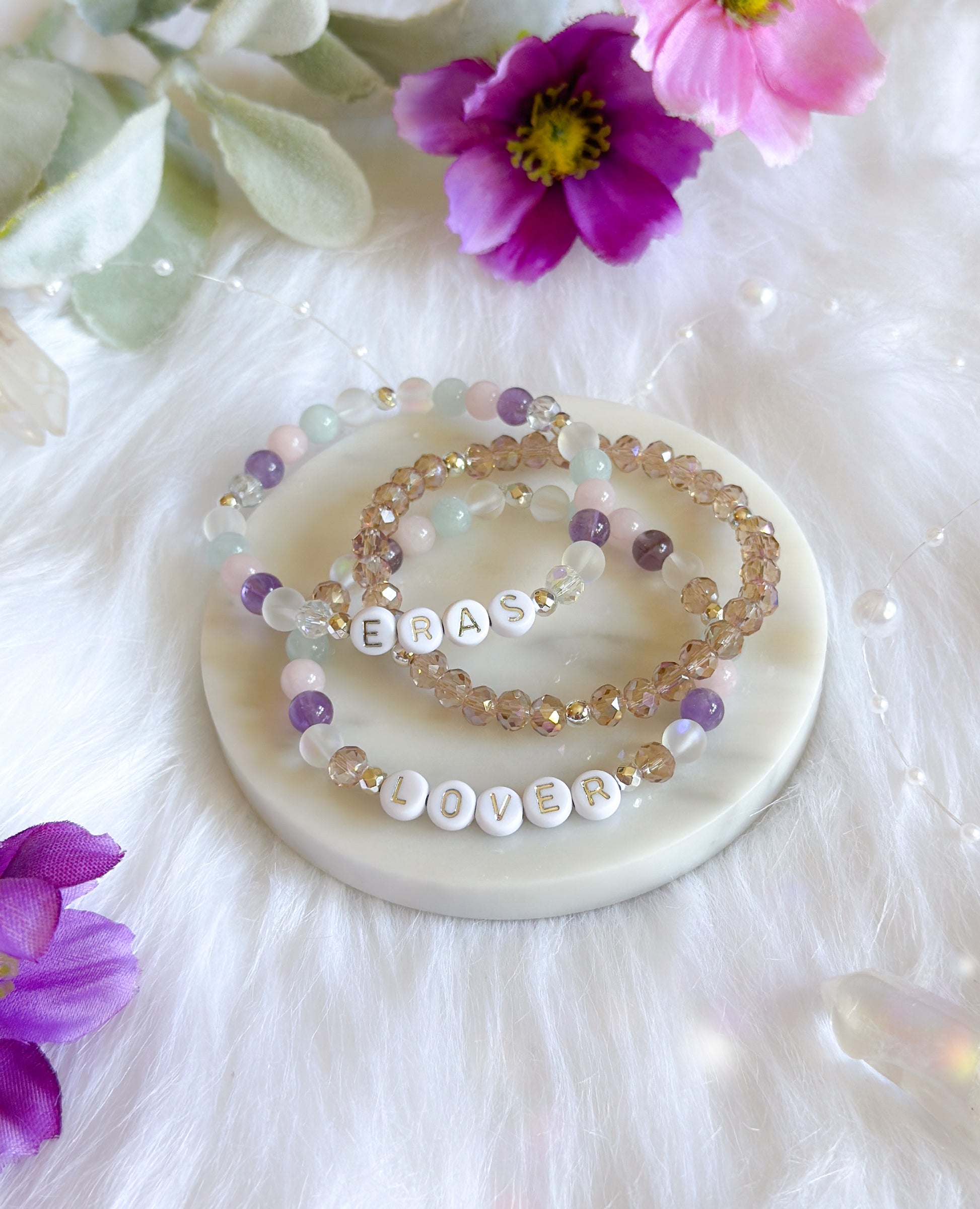 Introducing the Taylor Swift "Eras" Bracelet, a stunning piece crafted with Amethyst, Rose Quartz, Aura Quartz, Aquamarine, and sparkly glass beads. This bracelet is a tribute to Taylor Swift’s musical journey, designed for Swiftie fans who cherish her evolution as an artist. Each gemstone not only represents a unique chapter of Taylor's career but also brings its own healing properties.