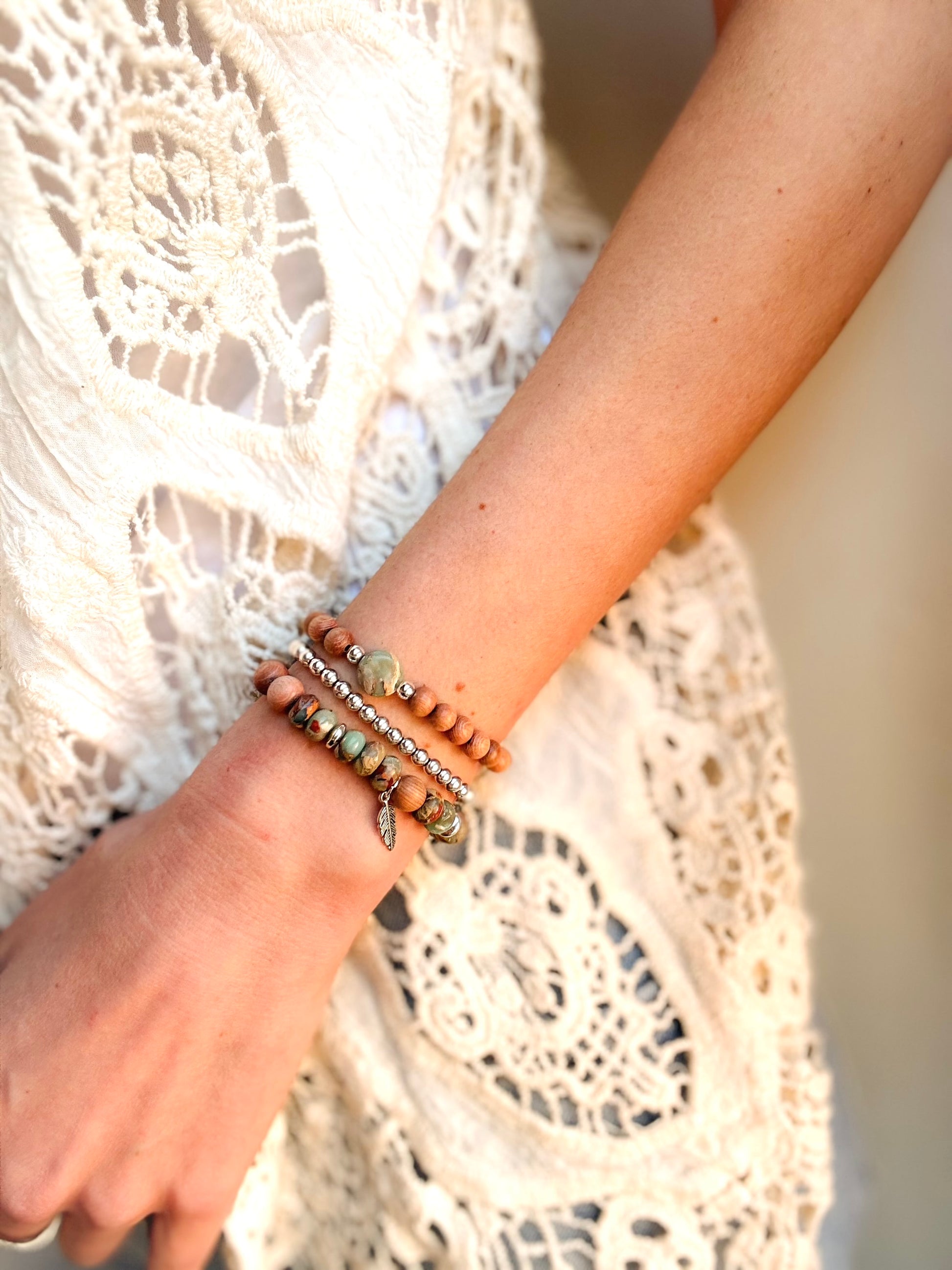 A handcrafted bracelet set featuring Serpentine Jasper beads in earthy green tones, symbolizing transformation and inner peace. Warm, natural Rosewood beads provide grounding energy, while a delicate feather charm dangles, representing freedom and intuition. Designed for free spirits and wanderers, this set embodies balance, resilience, and adventure.