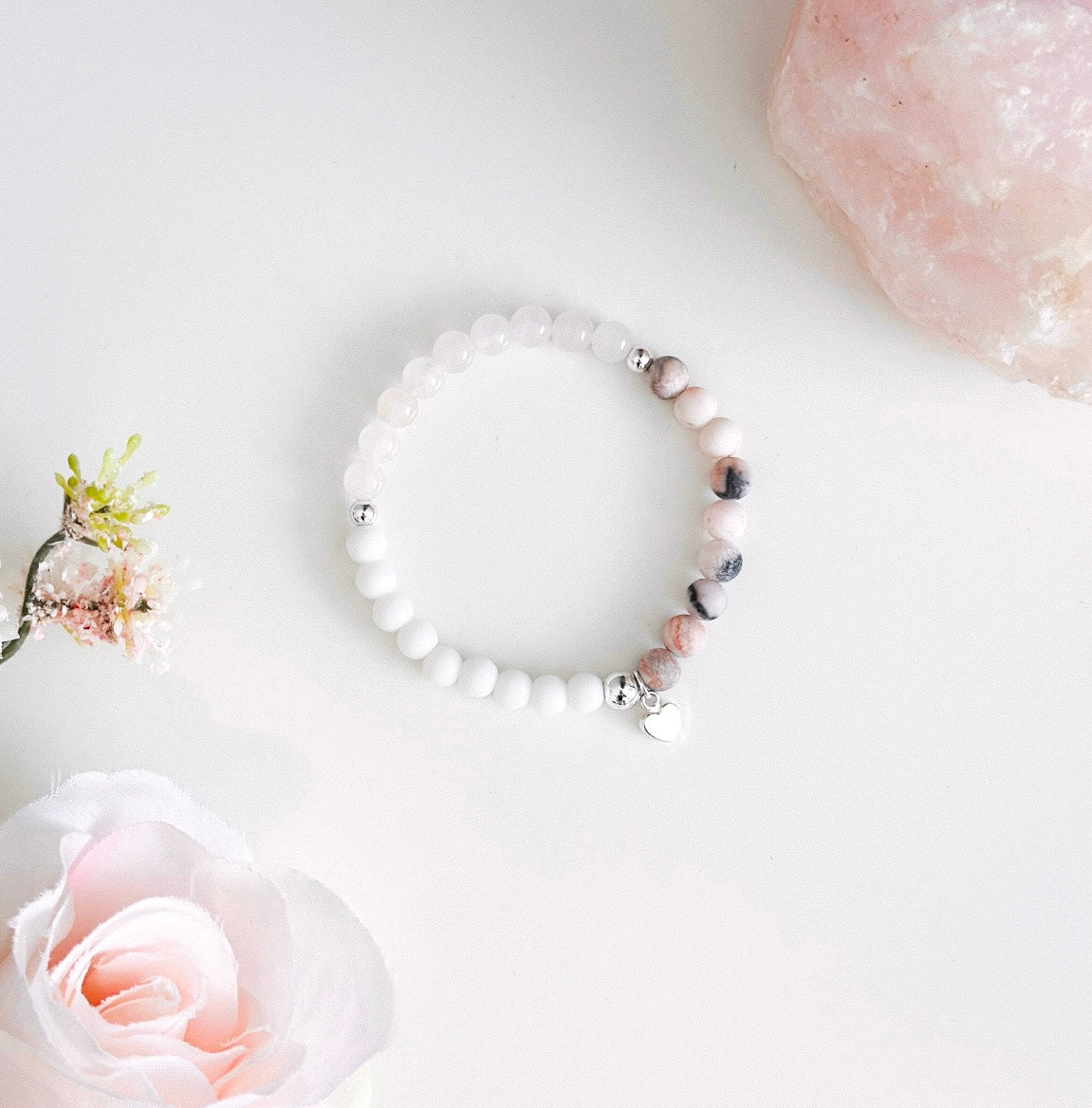 This exquisite gemstone bracelet blends the soothing energies of frosted Pink Zebra Jasper, the love-infused essence of Rose Quartz, and the calming properties of white agate. Crafted with care, it features a delicate silver heart charm, adding a touch of elegance to its design.