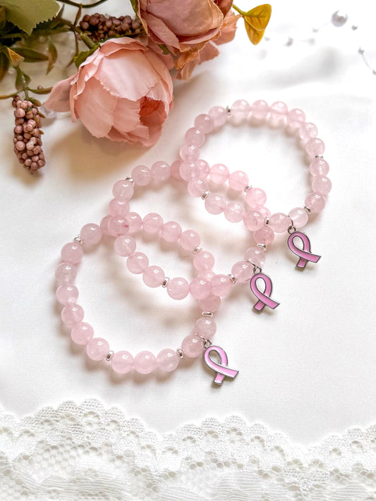 Pink beaded bracelets with breast cancer awareness ribbons on a white surface with flowers.