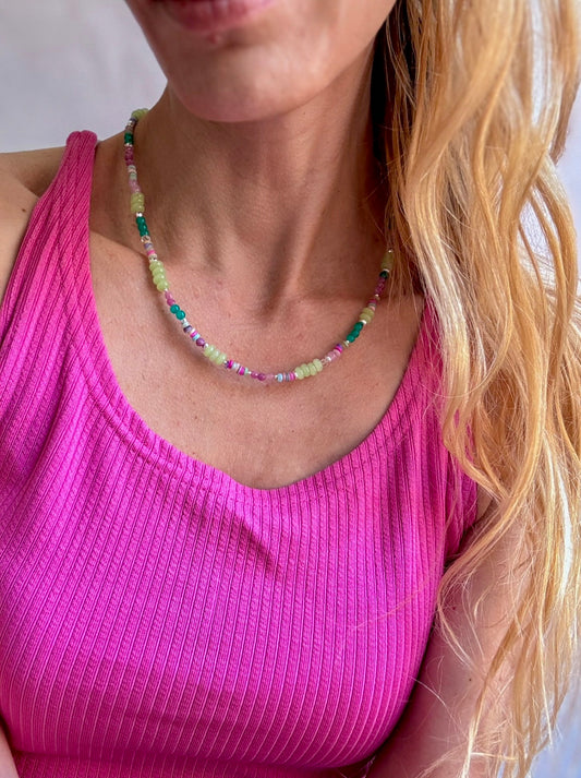 Person wearing a pink top and colorful beaded necklace against a neutral background