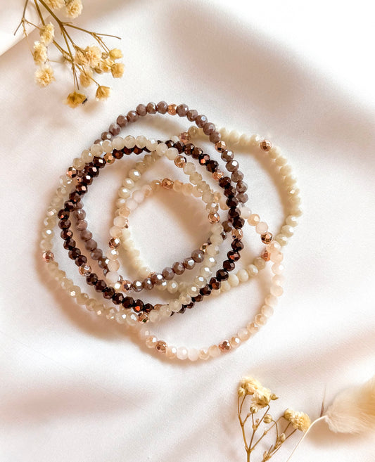 Five handcrafted gemstone bracelets from the Café Mocha Set arranged on a neutral-toned surface. The bracelets feature warm, earthy tones with subtle sparkling accents, evoking cozy fall vibes and comforting coffee and cocoa hues.