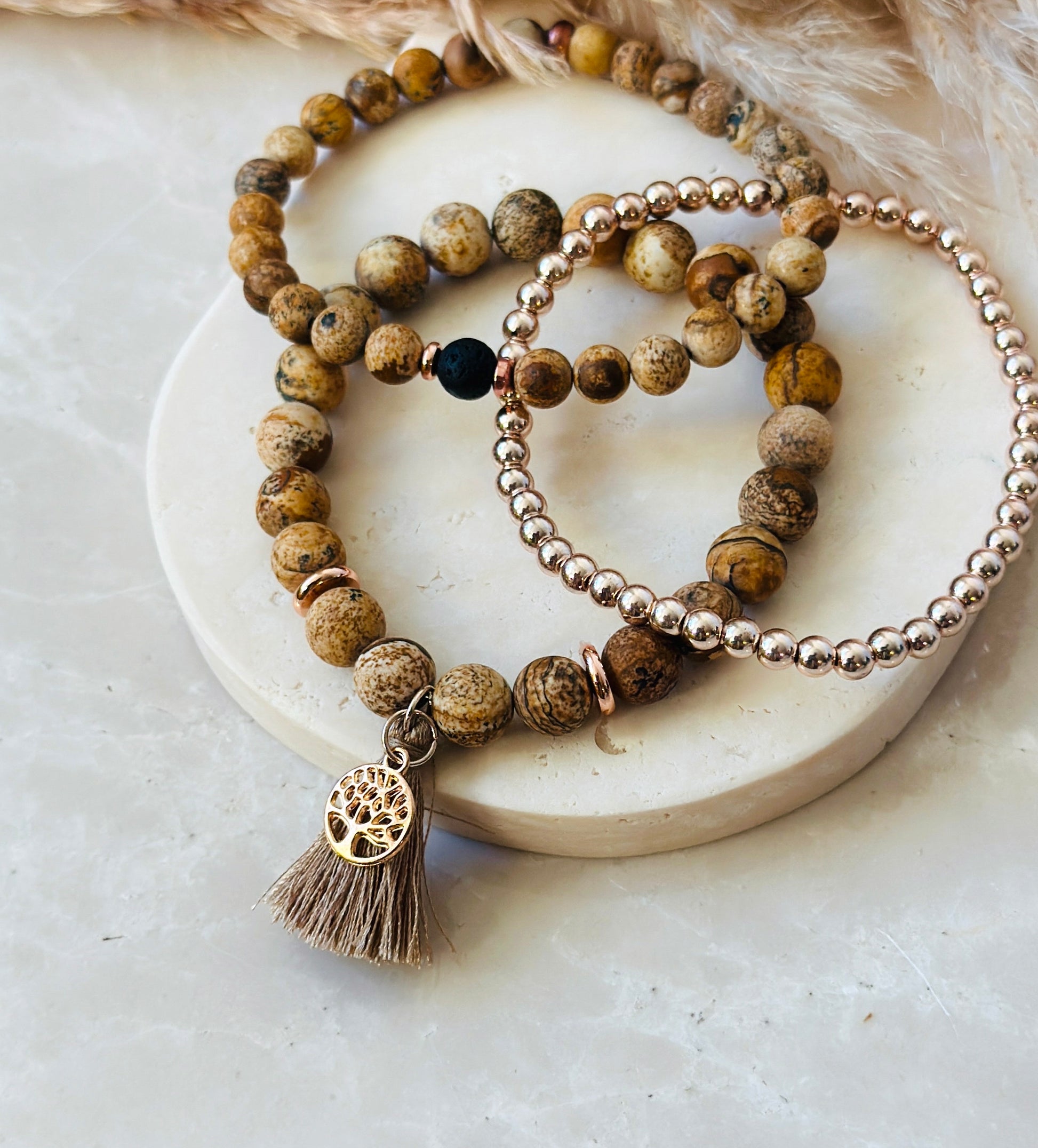 "The Sand Jasper Stack”  a unique gemstone bracelet ensemble meticulously crafted with the soothing and grounding qualities of Sand Jasper, a profound tree of life charm that embodies rich symbolism, and a practical tassel designed to infuse your days with the therapeutic fragrances of essential oils.