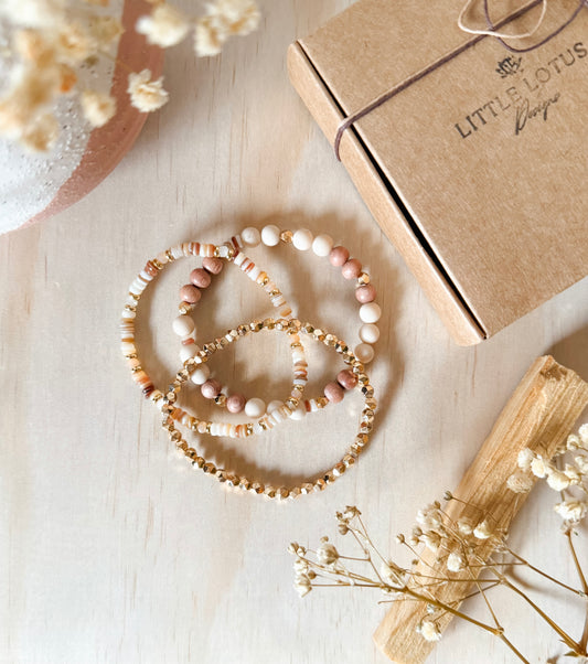 The Anira Bracelet Set — three handcrafted bracelets featuring neutral rondelle beads, faceted gold hematite, and a mix of river stone jasper, rosewood, and gold accents. Designed with earthy fall tones to evoke calm, balance, grounding, and autumn-inspired warmth.