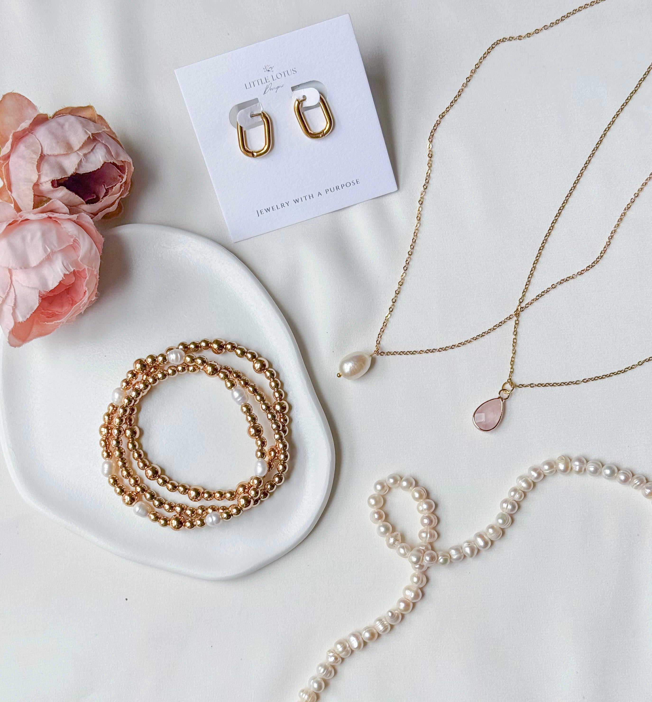 Mother's Day jewelry Collection including necklaces and bracelets on a white surface with pink flowers.