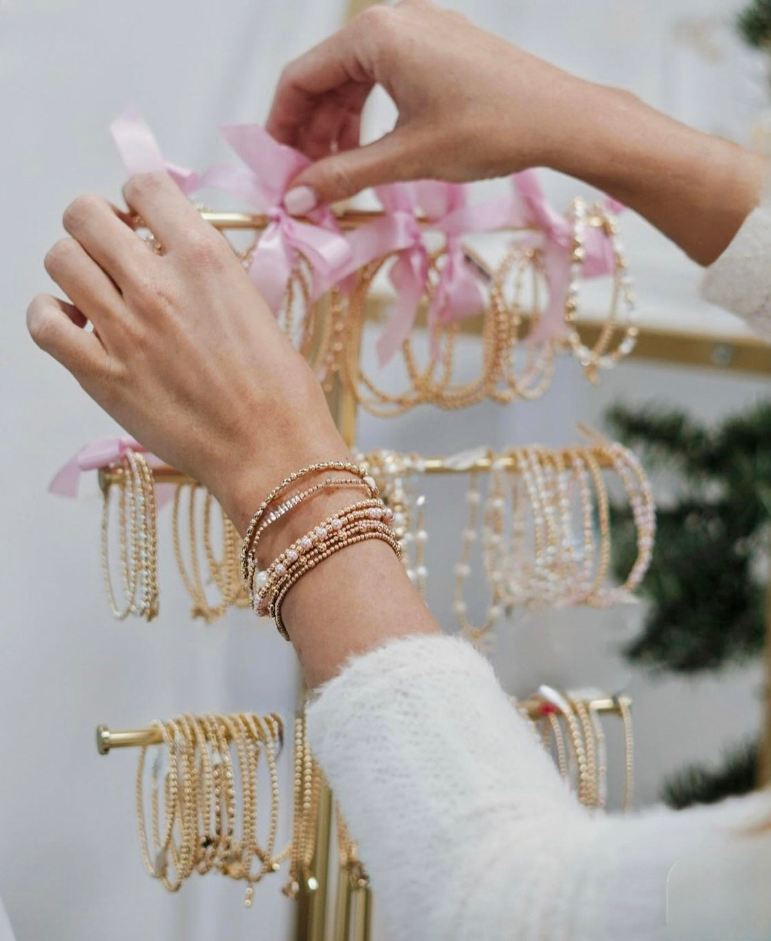 Person wearing gold bracelets with a jewelry stand in the background