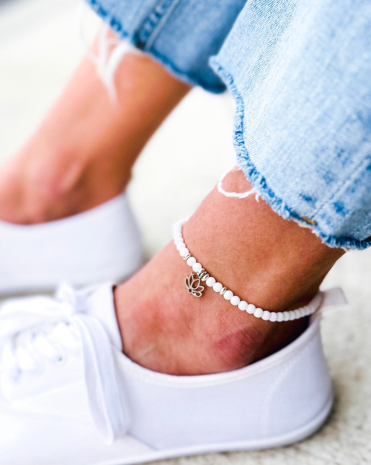 Person wearing a beaded anklet with a silver charm on a white sneaker.