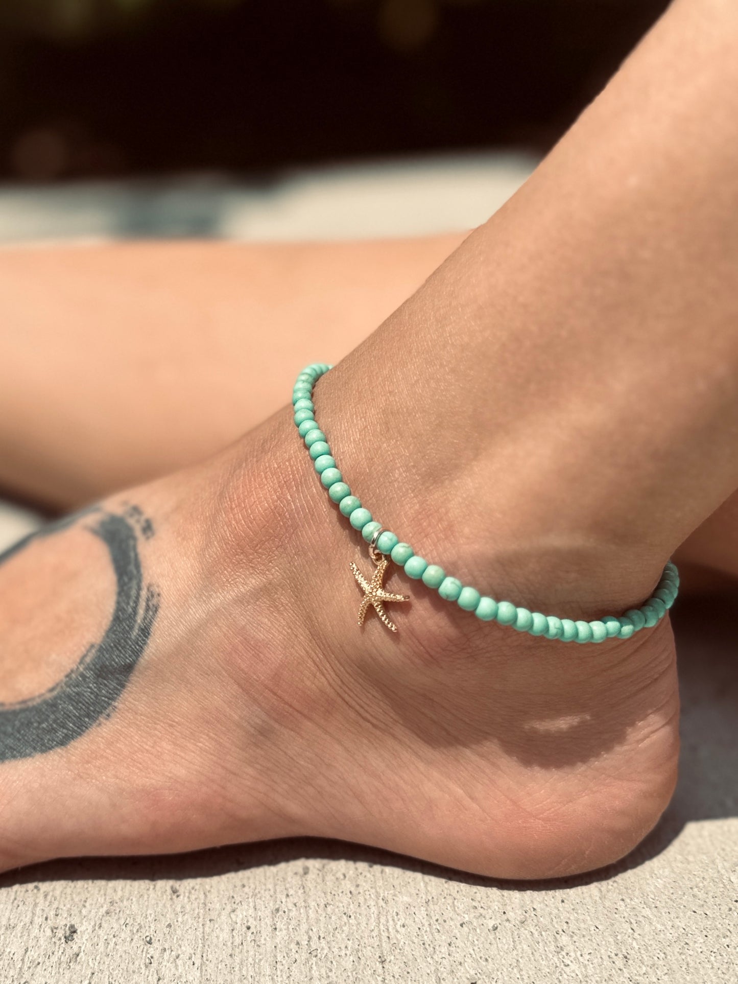 model wearing a sea foam green anklet on stretch cord with a gold starfish charm